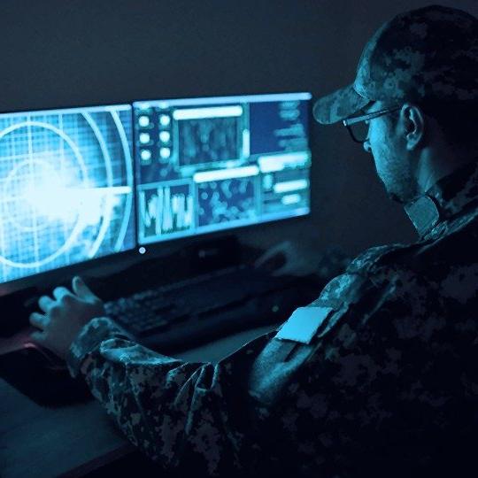 Man in green army uniform sitting at a computer protected by a government network security system